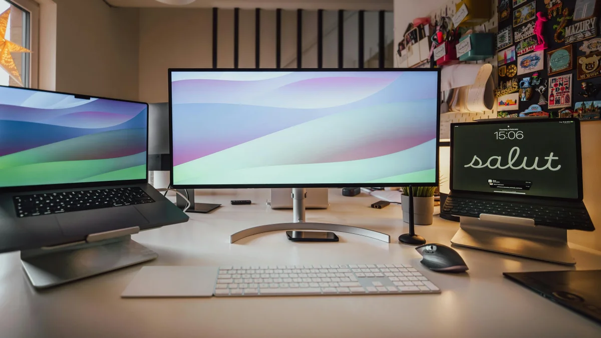 A clean workspace featuring two macbooks and an ultrawide monitor